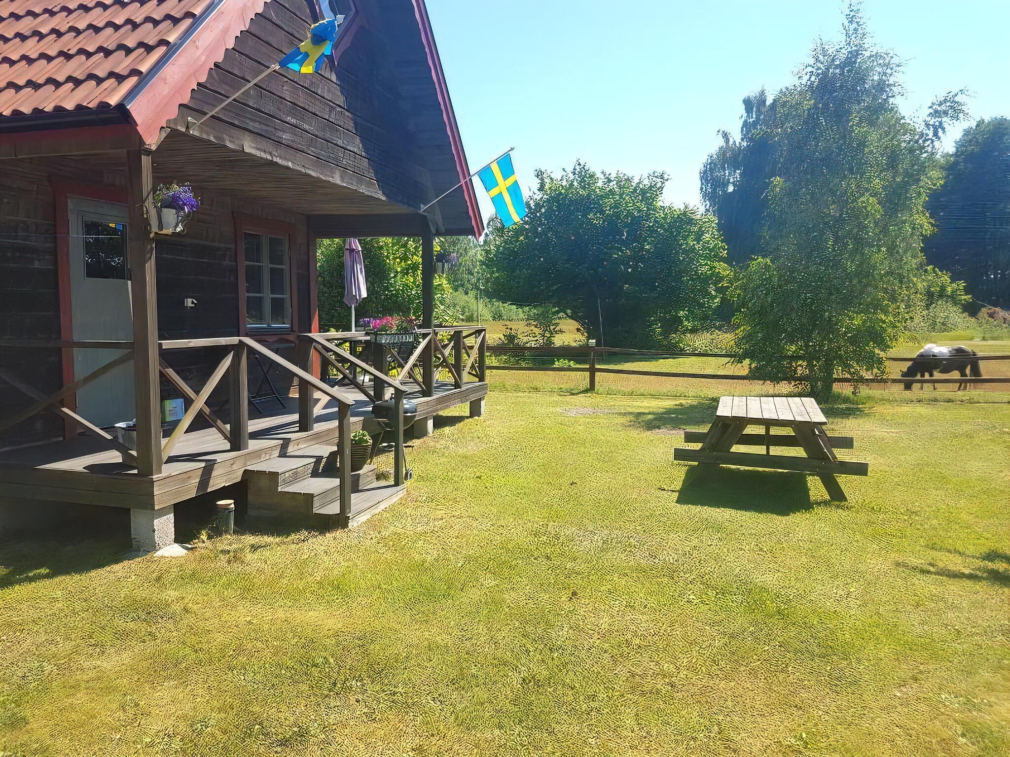 Une cabane en bois avec un porche, un drapeau et une table de pique-nique, le tout situé dans un espace verdoyant.