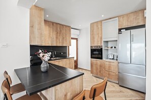 Eine moderne Küche mit Holzschränken, einer schwarzen Arbeitsplatte und einem Edelstahlkühlschrank.