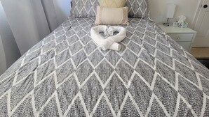 A neatly made bed with a patterned bedspread, a pillow, and a decorative swan-shaped pillow.
