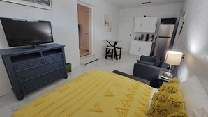 A hotel room with a bed, a TV, a desk, and a kitchenette.