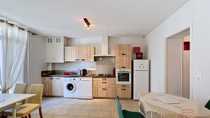 Eine kleine Küche mit Waschmaschine, Herd und Kühlschrank. Ein Essbereich mit Tisch und Stühlen ist ebenfalls vorhanden.