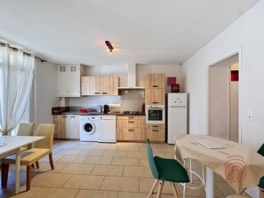Eine kleine Küche mit Waschmaschine, Herd und Kühlschrank. Ein Essbereich mit Tisch und Stühlen ist ebenfalls vorhanden.