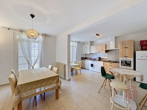 A modern kitchen with a washing machine, a dining area with a table and chairs, and a small kitchenette. - Charming well-located apartment - guests (Lamalou-les-Bains)