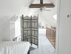 Ein Zimmer mit einem Bett, einem Deckenventilator, einer Holzwand und Blick ins Freie.
