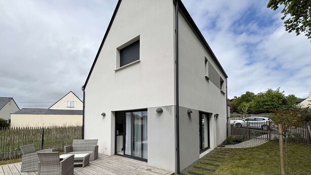 Een modern huis met twee verdiepingen, een houten terras en tuinmeubilair.