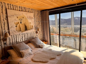 Ein Schlafzimmer mit einem großen Bett, Blick auf eine Brücke und einem Bärenbild an der Wand.