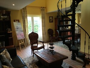 Ein Wohnzimmer mit Couch, Sessel, Holztisch, einem Gemälde auf einem Lehrstuhl, einer Treppe und einem Fenster mit Vorhängen.