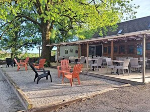 An outdoor seating area with chairs and tables, a covered patio, and a building in the background. - Mobile home terrace - 4 guests (Rocamadour)