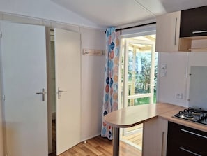Eine Küche mit einem Gasherd, Holzschränken und einem Fenster mit Vorhang.