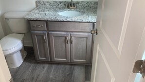 Un baño con inodoro blanco, lavamanos sobre encimera de granito y armarios de madera.