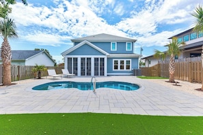 Una casa de dos pisos con piscina, patio trasero cercado y terraza de madera.