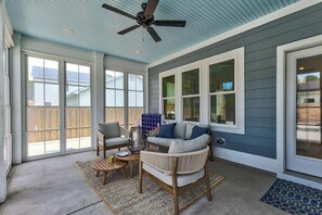 Eine überdachte Terrasse mit Deckenventilator, gepolsterten Sitzgelegenheiten und großen Fenstern.