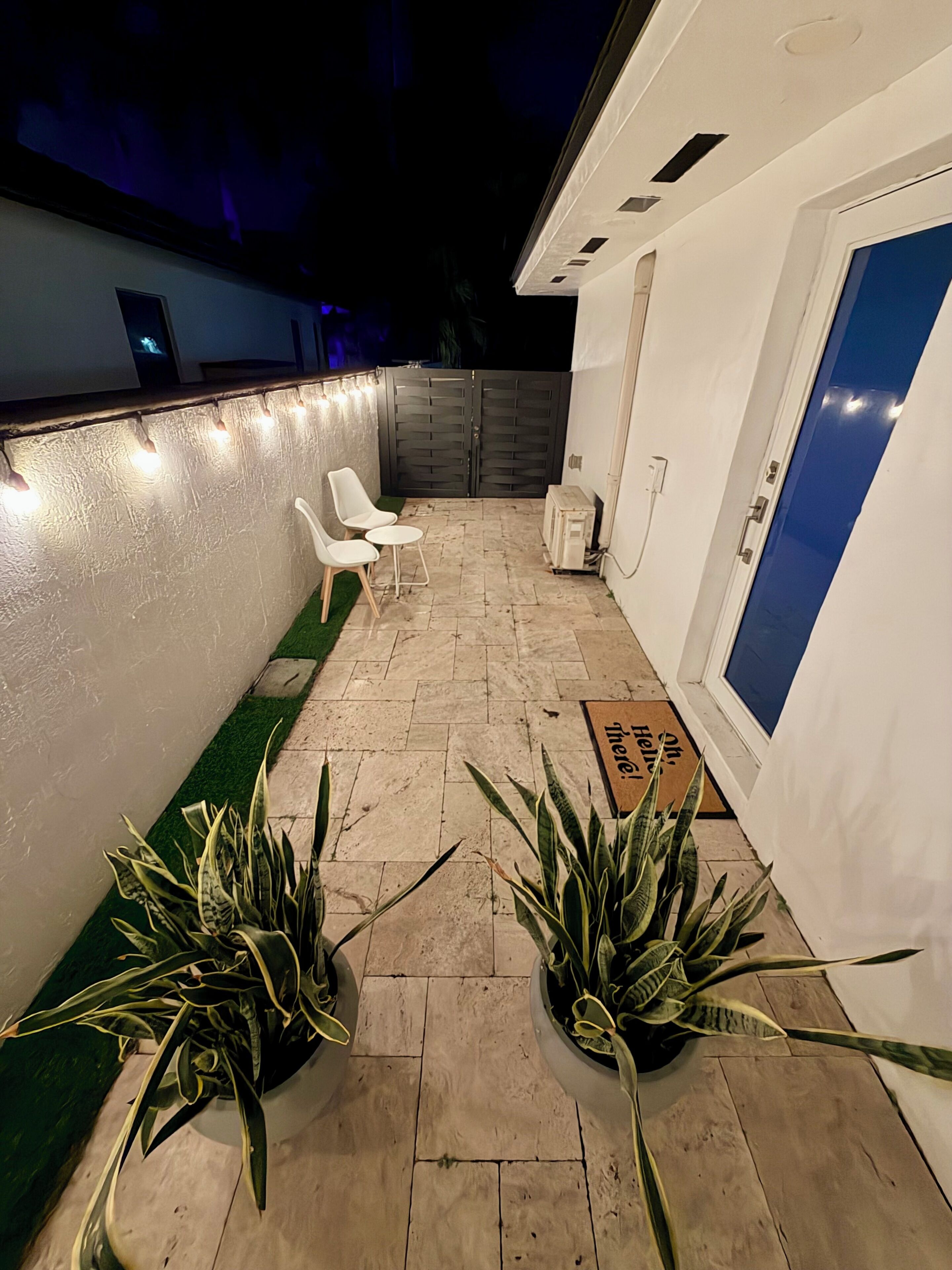 Une terrasse avec un espace salon, des plantes en pot, une porte et un mur bleu.