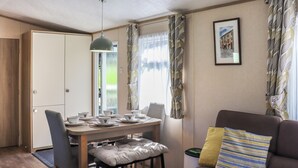 Une pièce avec une table à manger dressée pour quatre personnes, un canapé agrémenté d’un coussin à motifs, une suspension et un tableau encadré accroché au mur.