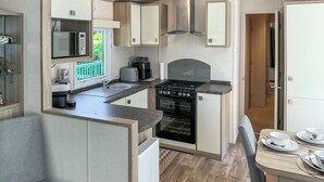 Une petite cuisine équipée avec une cuisinière, un évier et un four à micro-ondes, un coin repas avec une table pour deux personnes, et un petit espace salon.