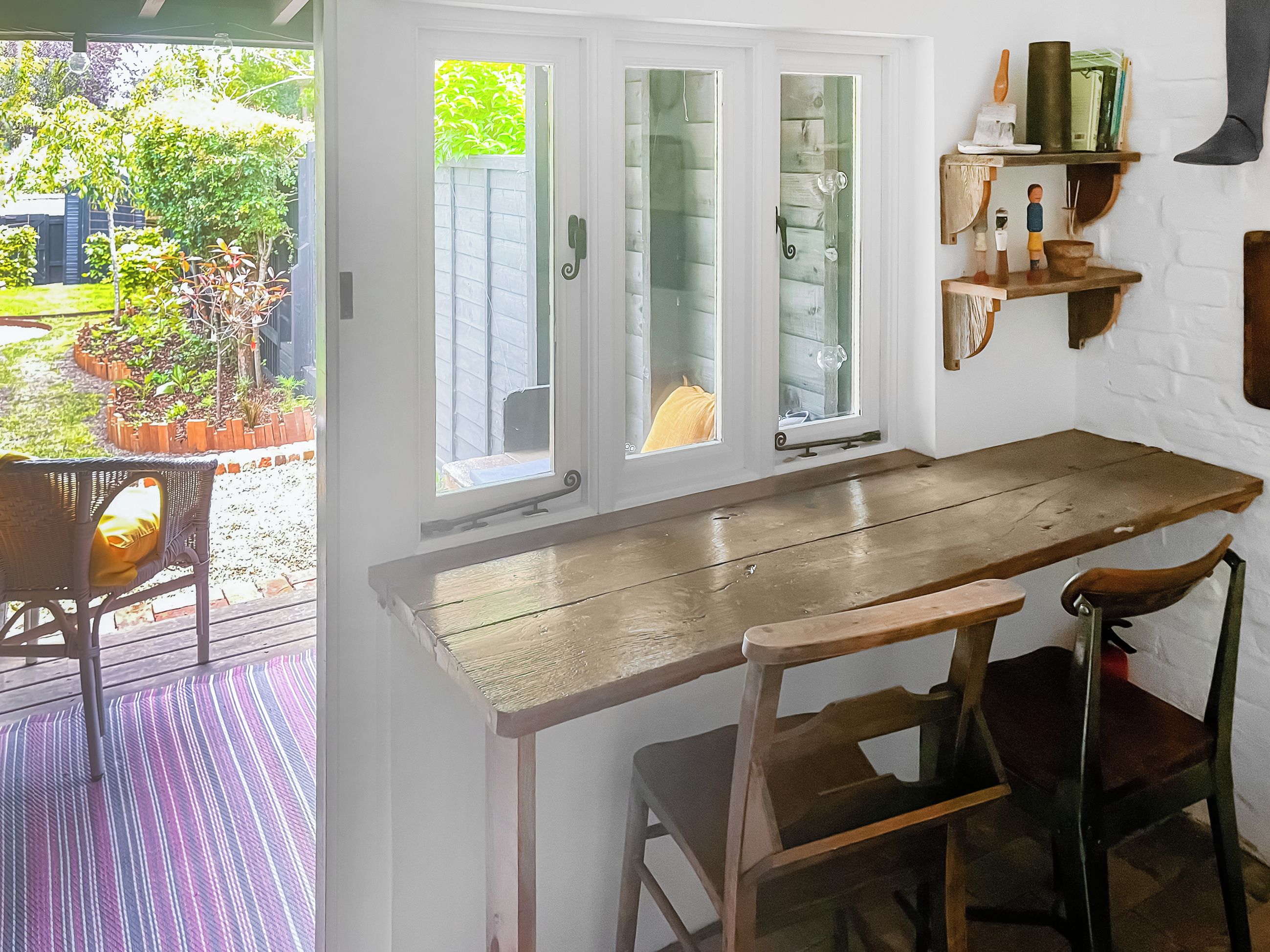 Een keuken met een houten tafel en stoelen, een raam met gezandstraald glas en een plank met keukengerei.