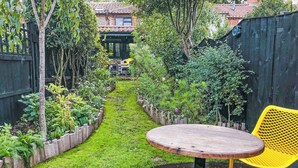 Ein Garten mit einem Weg, einem runden Holztisch und einem gelben Stuhl.