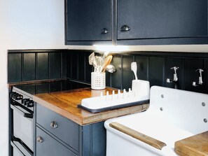 A kitchen with a wooden countertop, a white sink, and a stove. There are cabinets above the countertop and a backsplash. - 2 bedroom accommodation in Wenhaston (Wenhaston)