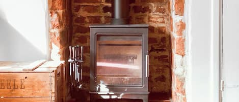 Una estufa de leña en una chimenea de ladrillo con un cofre de madera a su lado.