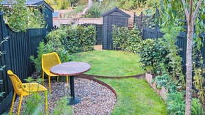 Ein Garten mit Holztisch und Stühlen, umgeben von einem schwarzen Zaun und verschiedenen Pflanzen.