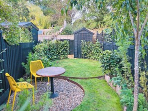 A garden with a wooden table and chairs, surrounded by a black fence and various plants. - 2 bedroom accommodation in Wenhaston (Wenhaston)