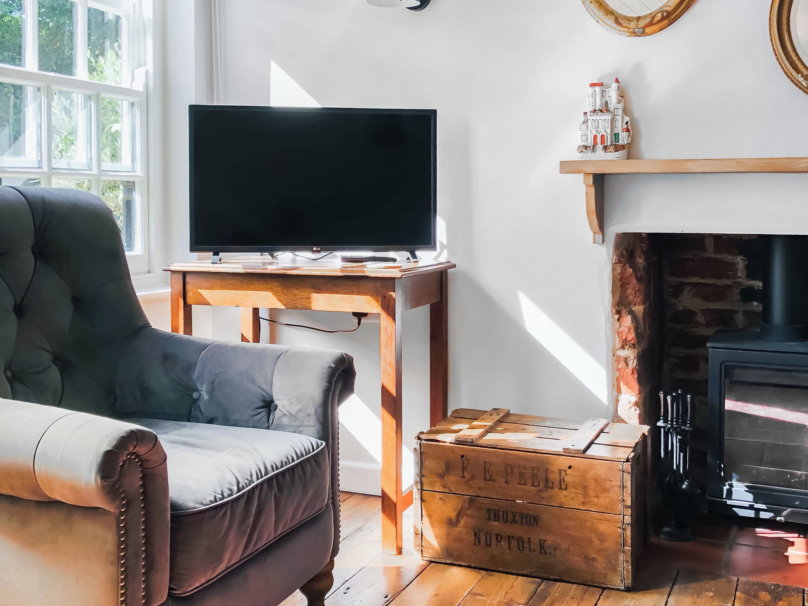 A living room with a leather sofa, a flat-screen TV on a wooden stand, a fireplace, and a vintage wooden chest.