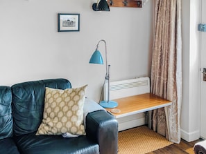 A room with a leather sofa, a small table, a floor lamp, a radiator, and a door with curtains. - 2 bedroom accommodation in Wenhaston (Wenhaston)