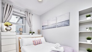Un dormitorio moderno con cama, mesitas de noche, una ventana con cortinas, un estante en la pared con plantas y un cuadro.