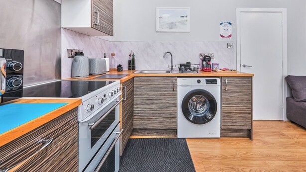 Una cocina compacta con horno empotrado, lavadora y cafetera.