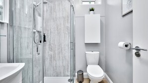 Un baño moderno con ducha envuelta en vidrio, inodoro, lavamanos y una pequeña planta en maceta.