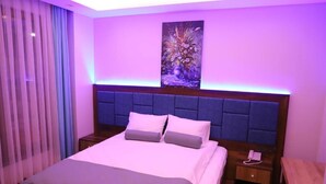 Habitación de hotel con cama, mesita de noche, cuadro en la pared y ventana con cortinas.