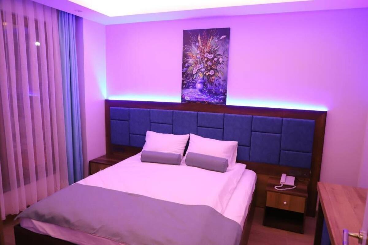 Habitación de hotel con cama, mesita de noche, cuadro en la pared y ventana con cortinas.
