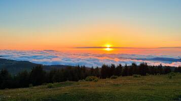 Un lever de soleil sur une chaîne de montagnes boisées, avec une vue sur le soleil au-dessus des nuages.