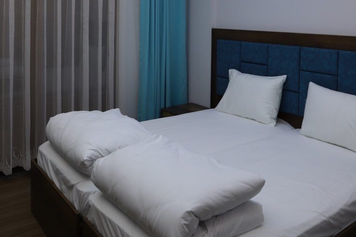 Una habitación de hotel con cama, cabecera y vista al cielo a través de una ventana.