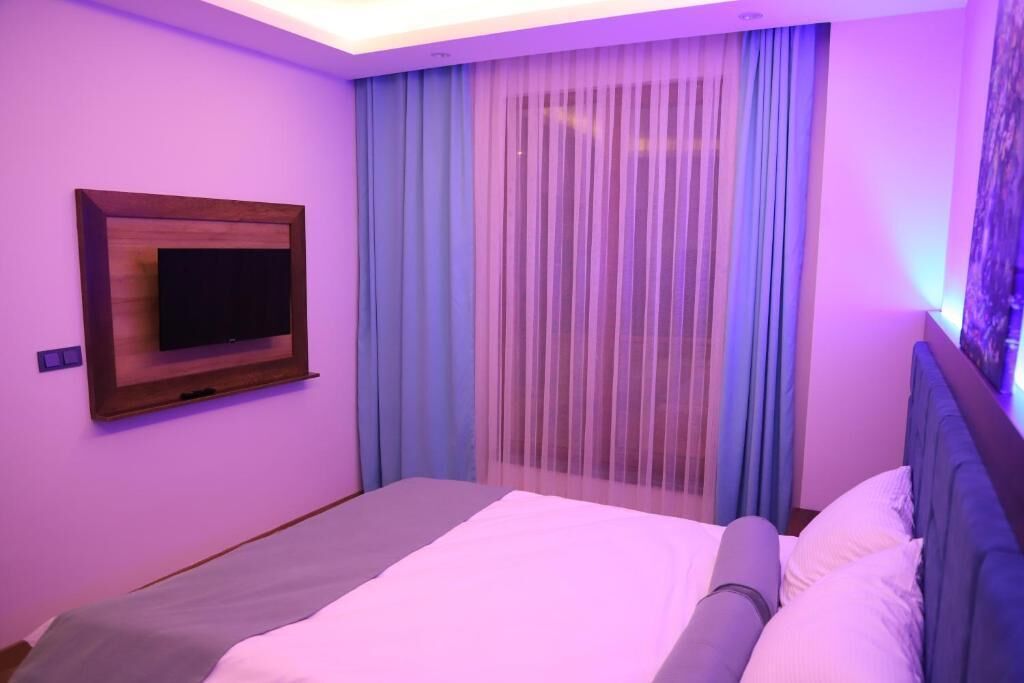 A bedroom with a bed, a mounted TV, and sheer curtains.