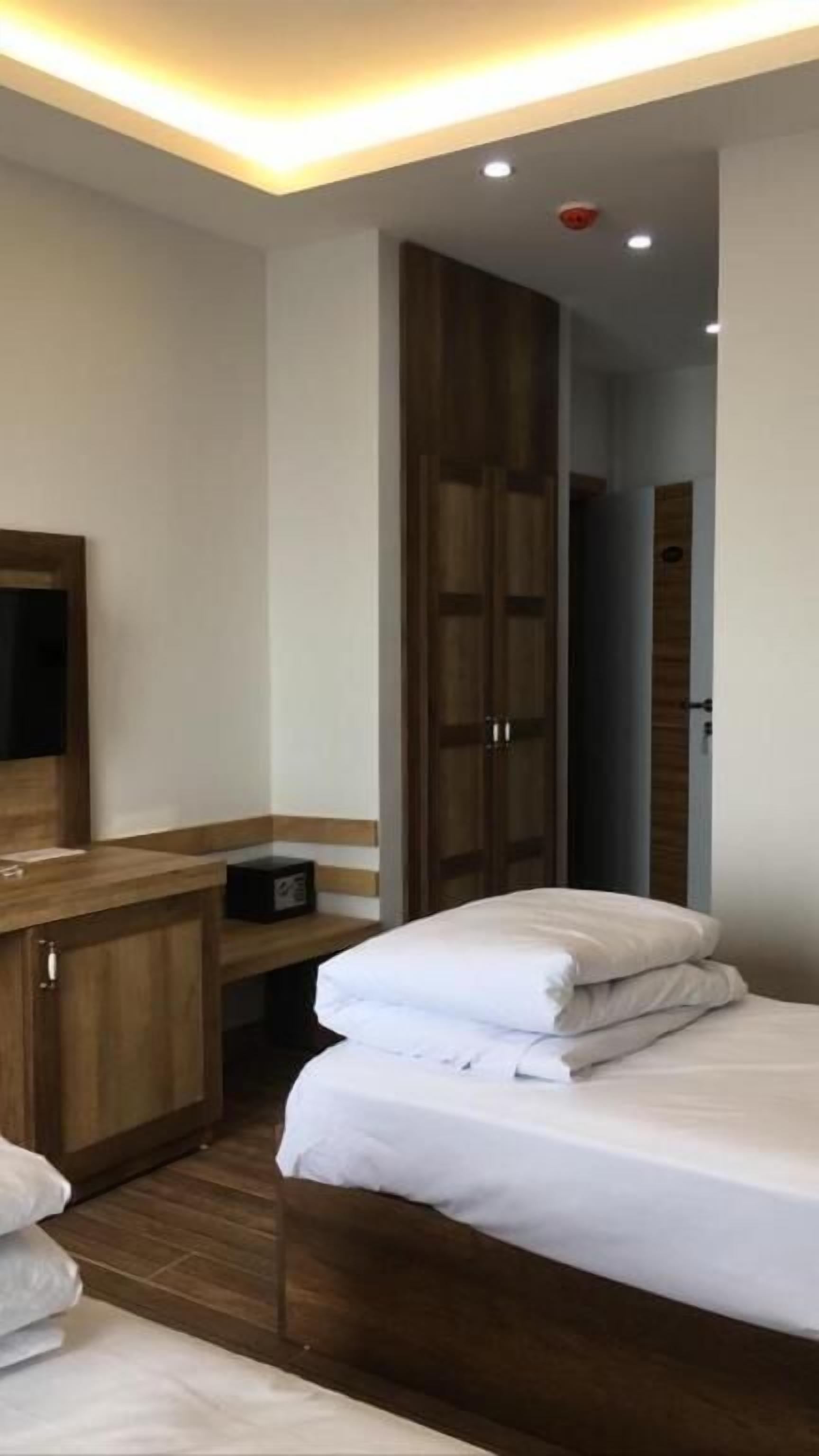 A hotel room with a bed, a desk with a chair, a wardrobe, and a mirror.