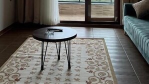 Una habitación con sofá, una mesa, un tapete estampado y un ventanal corredero que da a un balcón con vistas a la montaña.