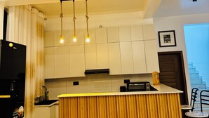 Une cuisine moderne dotée d’un îlot central, de luminaires suspendus et offrant une vue sur l’espace de vie, avec un canapé et des fauteuils.