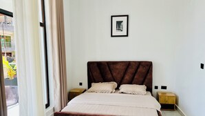 Une chambre à coucher avec un grand lit, deux tables de chevet, un tableau encadré au mur et une vue par la fenêtre.