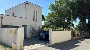 Un edificio moderno de dos pisos con entrada protegida por una reja, un automóvil estacionado y un pequeño jardín.