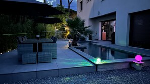 Zona de piscina exterior con un comedor y sombrillas, rodeada por un edificio moderno.
