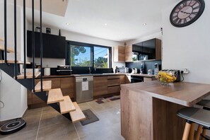 A modern kitchen with wooden cabinetry, a built-in dishwasher, and a large window providing natural light. - Villa Harmonie with Private Pool, Wi-Fi, and Air Conditioning (Bagnols-sur-Cèze)
