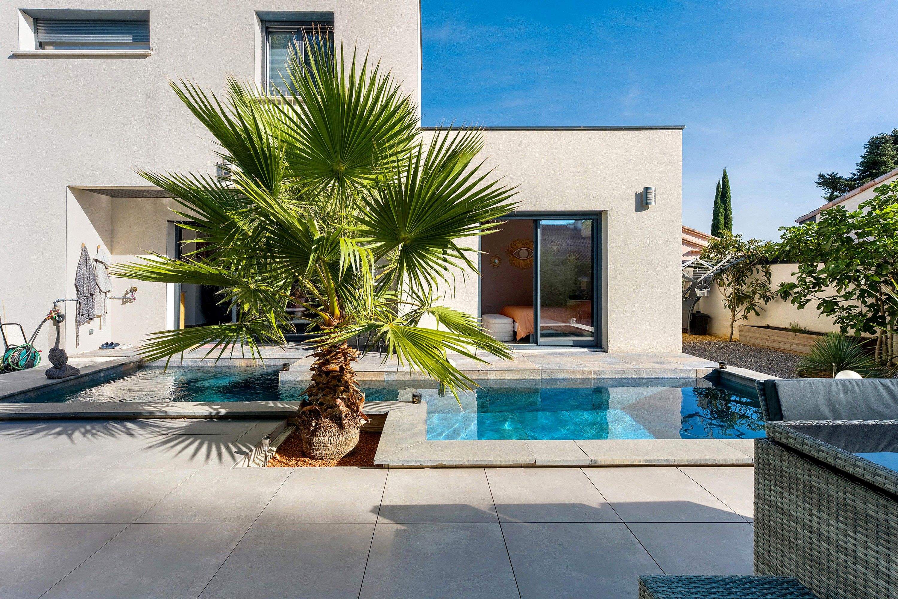A modern house with a swimming pool, a palm tree, and a clear blue sky.