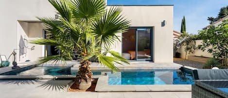 Una casa moderna con piscina, una palmera y un cielo azul despejado.