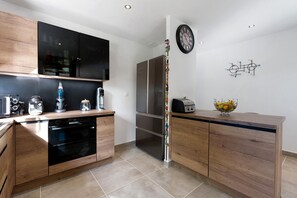 Eine moderne Küche mit Holzausstattung, einem Einbauofen, einem Kühlschrank, einer Wanduhr und einer Obstschale auf der Arbeitsfläche.