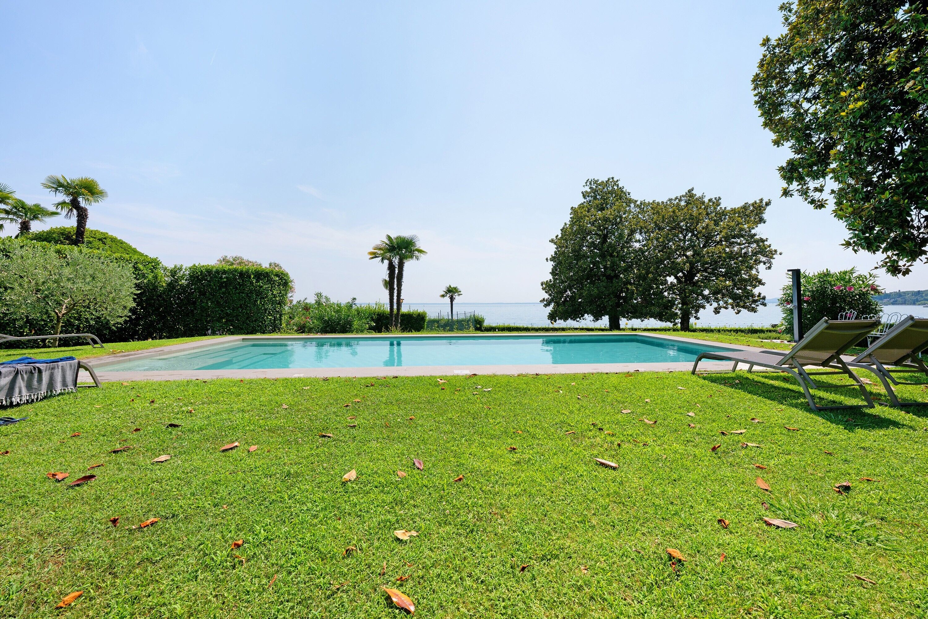 Una piscina con vista al mar, rodeada de césped y árboles.