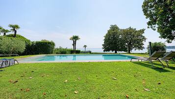 Una piscina con vista al mar, rodeada de césped y árboles.