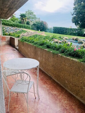 A patio with a white metal table and chairs, a concrete wall with greenery, and a view of a landscaped garden. - Apartment 'Appartamento Alessandra' with Lake View, Wi-Fi and Air Conditioning (Garda)