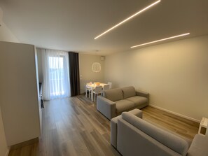 A modern living room with a sofa, a dining table, and a kitchen area. - Apartment 'Appartamento Alessandra' with Lake View, Wi-Fi and Air Conditioning (Garda)