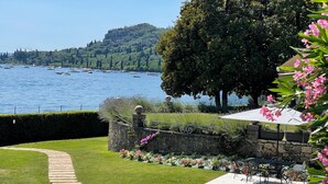 Ein angelegter Garten mit einer Steinmauer, einem gepflasterten Weg und Blick auf Boote auf dem Wasser.